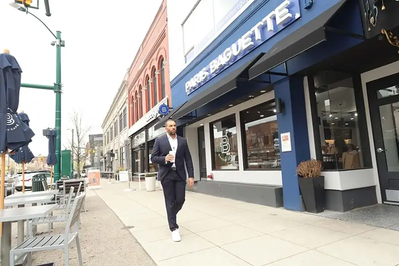 Randy walking down street in front of Paris Baguette with coffee